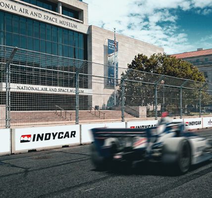 Carro da IndyCar em alta velocidade passando em frente ao National Air and Space Museum no circuito de rua de Washington, DC.