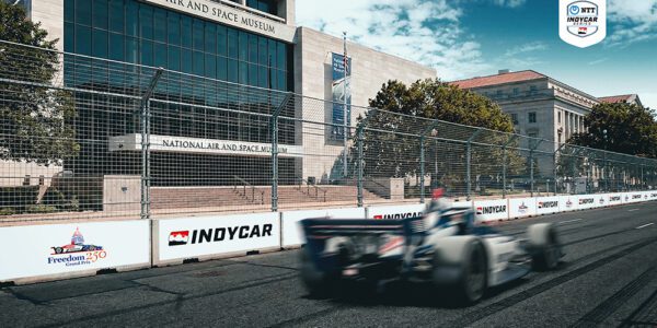 Carro da IndyCar em alta velocidade passando em frente ao National Air and Space Museum no circuito de rua de Washington, DC.